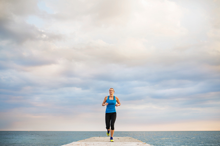 A young sporty woman running on a pier by the ocean outside.の写真素材