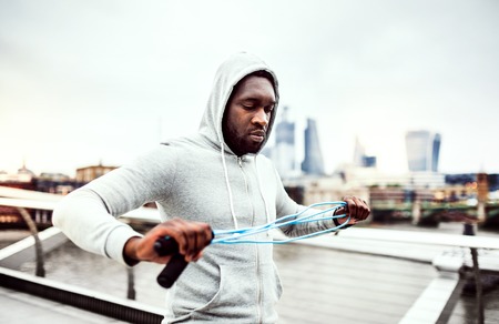 Young active black sportsman with skipping rope in a city, wearing hoodie.の写真素材
