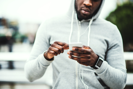 Black man runner with smart watch and smartphone on the bridge in a city, resting.の写真素材