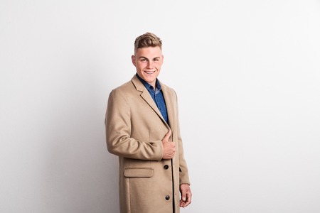 Portrait of happy young man in a studio, wearing brown coat. Copy space.の写真素材