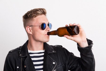 A confident young man with sunglasses in a studio, drinking beer from bottle.の写真素材