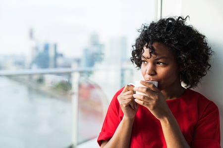 A close-up of a woman standing by the window drinking coffee.の写真素材