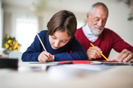 A small girl and her grandfather writing Christmas cards together.の写真素材