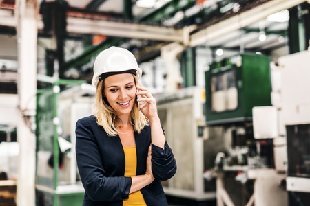 A portrait of an industrial woman engineer on the phone, standing in a factory.の写真素材