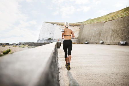 A rear view of young sporty woman runner running outside on a beach in nature.の写真素材