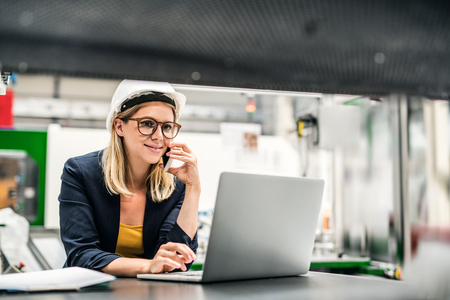 A portrait of an industrial woman engineer in a factory using laptop and smartphone.の写真素材