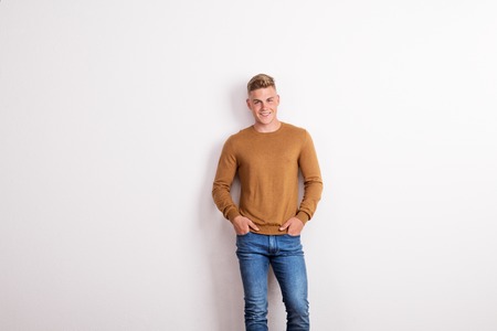 Portrait of a happy young man standing in a studio, hands in pockets.の写真素材