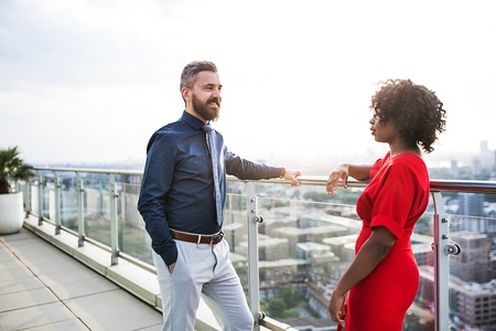 A portrait of two businesspeople standing against London view panorama, talking.