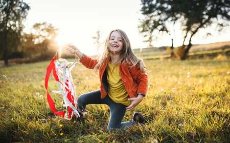 A small girl playing with a rainbow hand kite in autumn nature at sunset.の写真素材