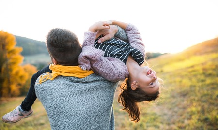 A rear view of young father having fun with a small daughter in autumn nature.の写真素材