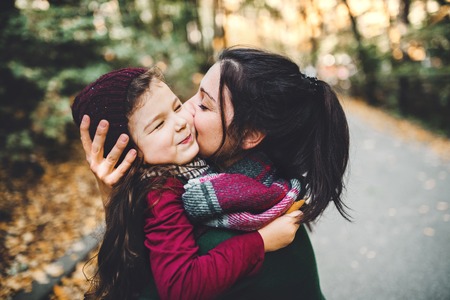 A young mother with a toddler daughter hugging and kissing in forest in autumn nature.の写真素材