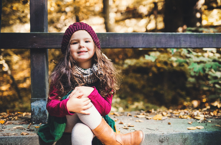 A portrait of a small toddler girl sitting in forest in autumn nature.の写真素材