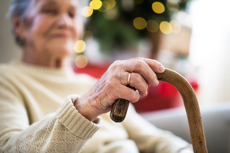 A close-up of a senior woman holding a walking stick at home at Christmas time.の写真素材