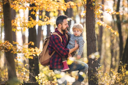 A mature father with a toddler son on a walk in an autumn forest.の写真素材