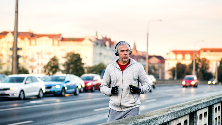 Mature male runner with headphones running outdoors on the bridge in Prague city.