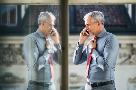Mature businessman with smartphone standing on a terrace in city, making a phone call.
