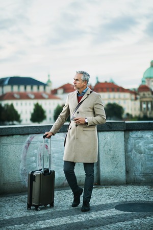 Mature businessman with suitcase standing on a bridge in Prague city.の写真素材