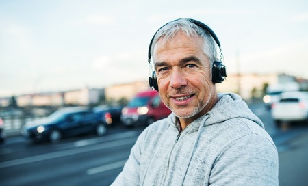 Mature male runner with headphones outdoors in city, listening to music.の写真素材