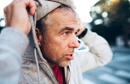 A portrait of an active mature man standing outdoors in city, putting on hood.の写真素材