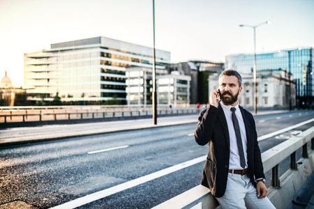 Hipster businessman with smartphone standing outdoors in the city.の写真素材