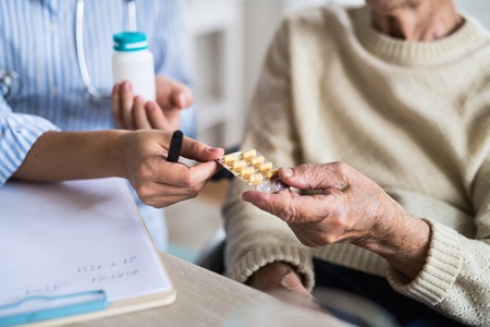 An unrecognizable health visitor explaining a senior woman in wheelchair how to take pills.