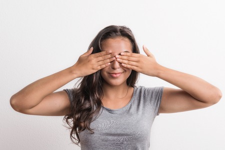 Young beautiful happy woman in studio, covering her eyes.の写真素材