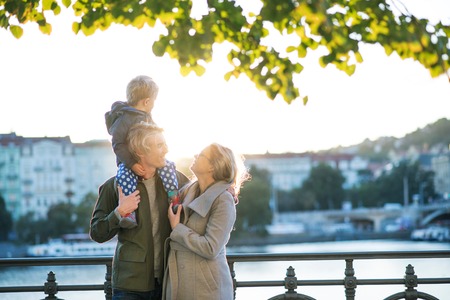 Young parents with their toddler son standing outdoors by the river in city at sunset.の写真素材
