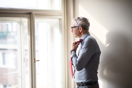 Mature businessman on a business trip standing in a hotel room, getting dressed.の写真素材