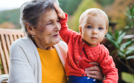 Elderly woman sitting with a toddler great-grandchild on a terrace in autumn.の写真素材