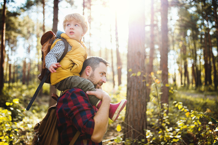 A mature father giving a toddler son a piggyback ride in an autumn forest.の写真素材