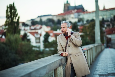 Businessman with smartphone standing on a bridge in city, making a phone call.の写真素材