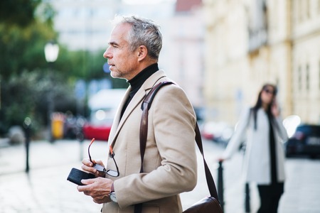 Mature businessman standing on a street in city, holding glasses.の写真素材