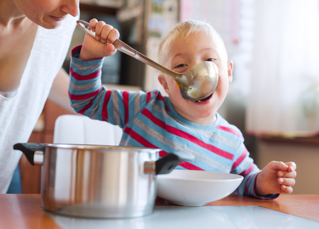 A handicapped down syndrome boy eating soup from a ladle indoors, lunch time.の写真素材