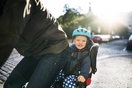A small toddler boy sitting in bicycle seat with father outdoors in city.の写真素材
