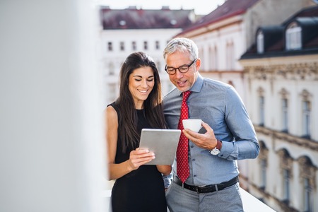 Man and woman business partners with tablet standing on a terrace in city, talking.の写真素材