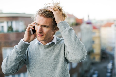 Young man with smartphone standing on a balcony in city, making a phone call.の写真素材