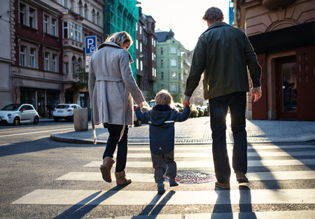 A rear view of small toddler boy with parents crossing a road outdoors in city.の写真素材