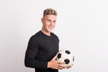 Portrait of a young man with football ball in a studio. Copy space.の写真素材