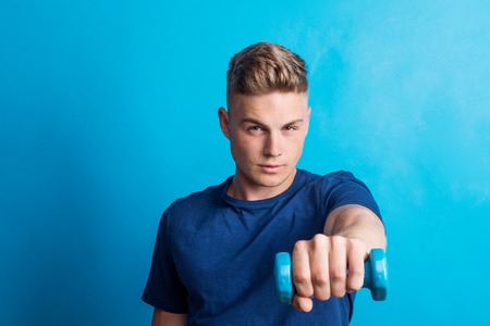 Portrait of a young man holding a dumbbell in a studio.の写真素材