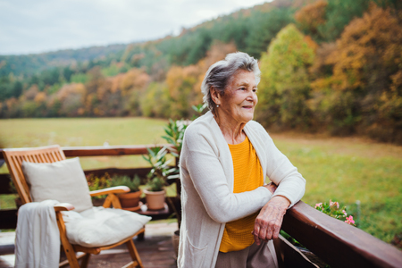 An elderly woman standing outdoors on a terrace on a sunny day in autumn.の写真素材