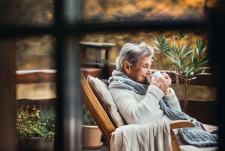 An elderly woman sitting outdoors on a terrace in on a day in autumn, drinking coffee.の写真素材