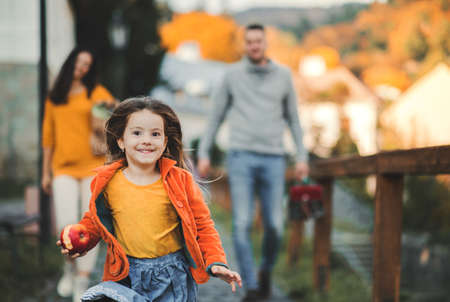 Small girl with unrecognizable parents in the background running in park in autumn.の写真素材