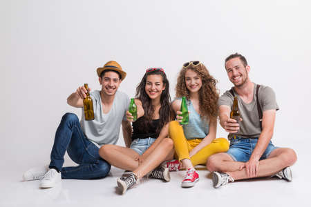Portrait of joyful young group of friends with bottles sitting on the ground in a studio.の写真素材