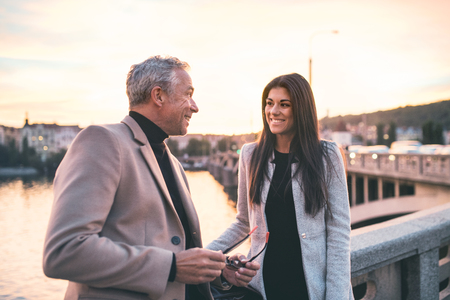 Man and woman business partners standing by a river in city at dusk, talking.の写真素材