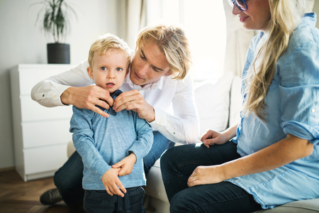 Young parents dressing their toddler son inside in a bedroom.の写真素材