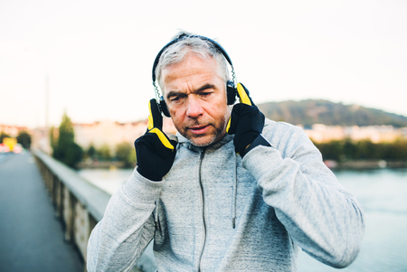 Mature male runner putting on headphones outdoors in city.の写真素材