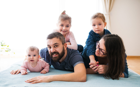 A portrait of young family with small children lying on floor indoors.の写真素材