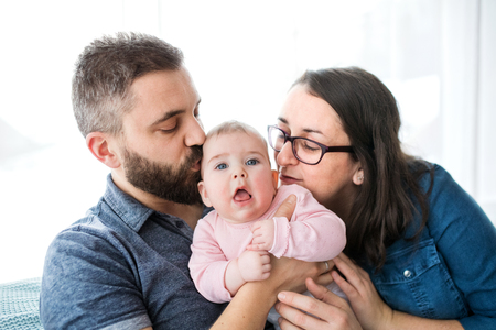 Portrait of young family with baby daughter sitting indoors on a sofa, kissing her.の写真素材