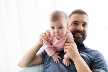 Portrait of young father with baby daughter sitting indoors on a sofa.の写真素材