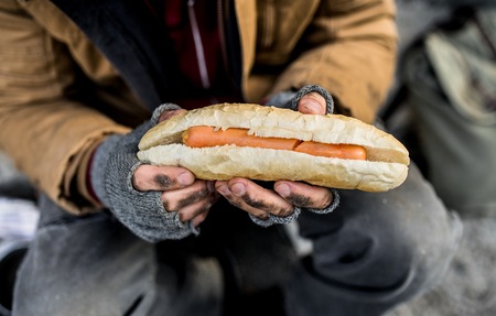 A midsection view of homeless beggar man outdoors in city, holding hot-dog.の写真素材